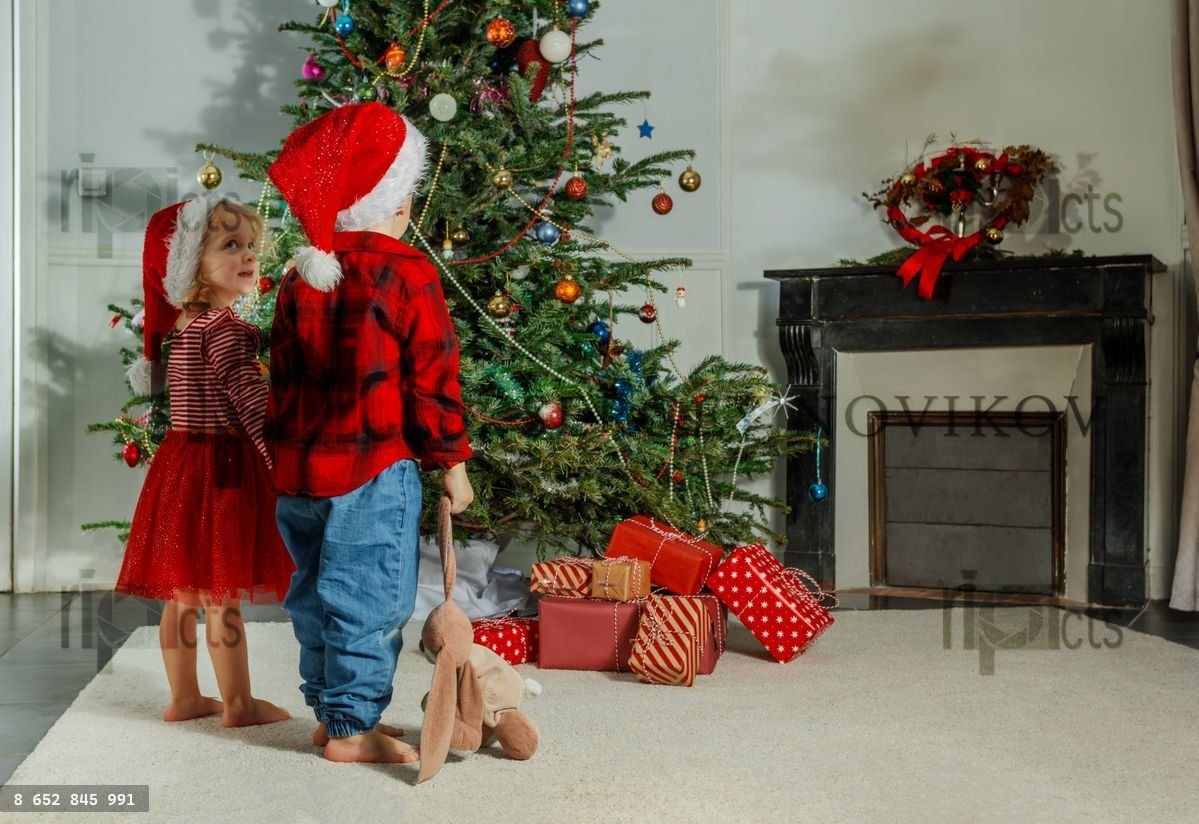 Small children in Santa hats admire a decorated Christmas tree