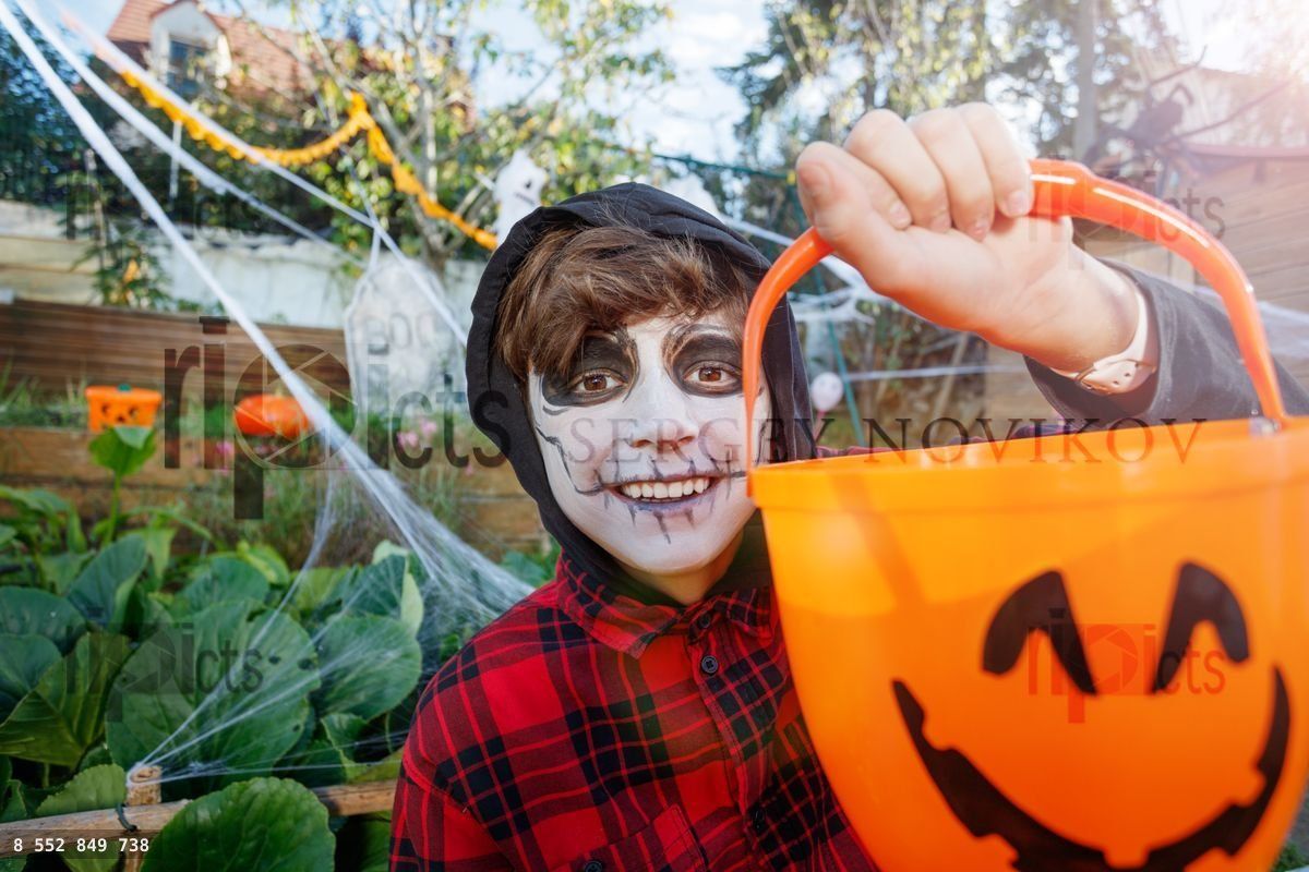 Close up of skeleton faced kid smile with Halloween candy bucket