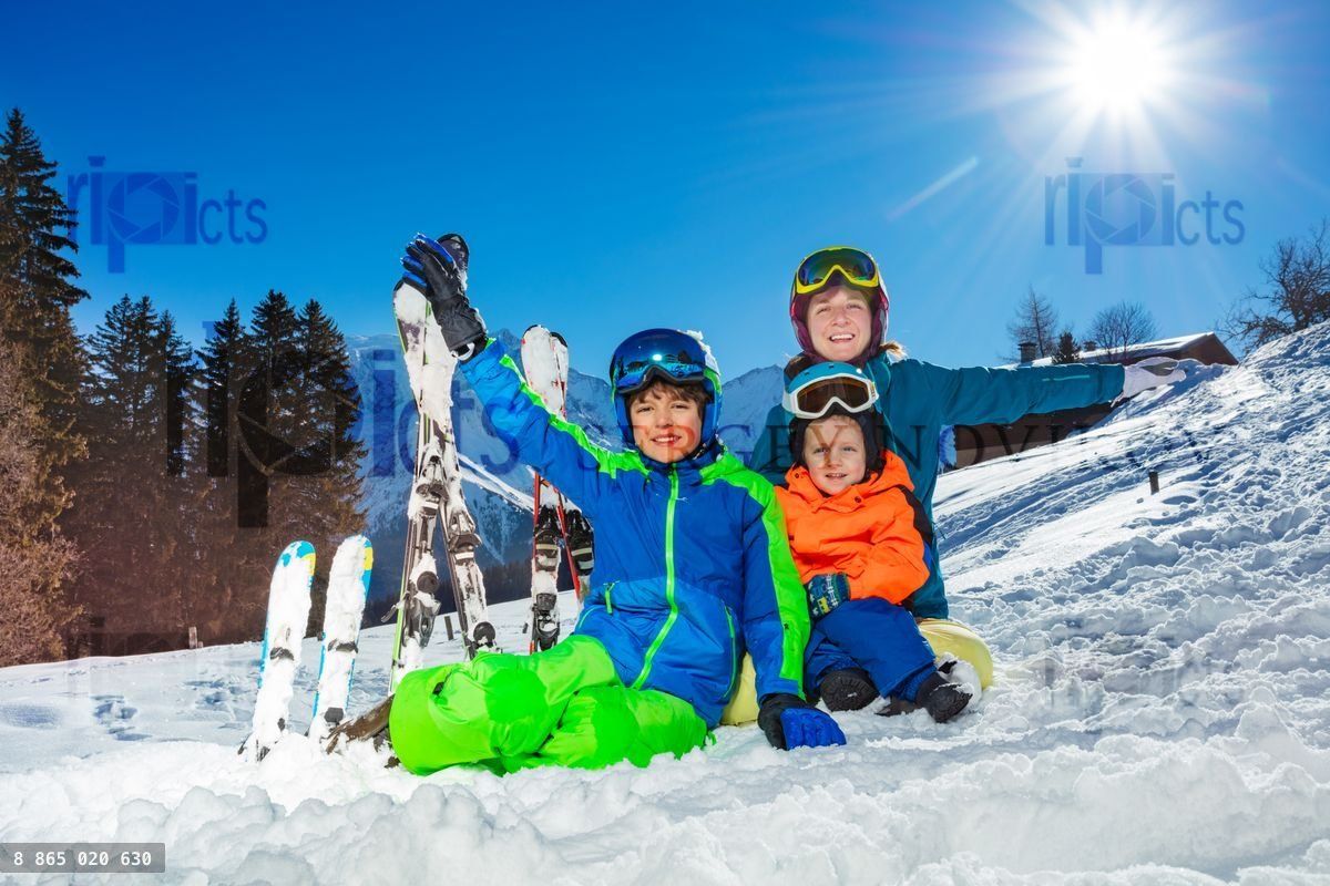 Two kids and mother on ski vacation sit together in the snow