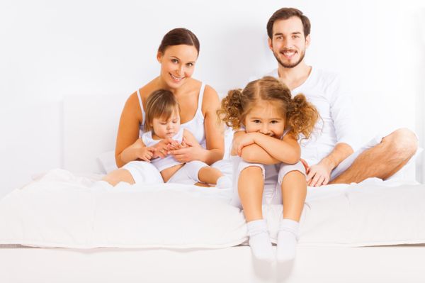 Family sitting on white bed in pajamas together