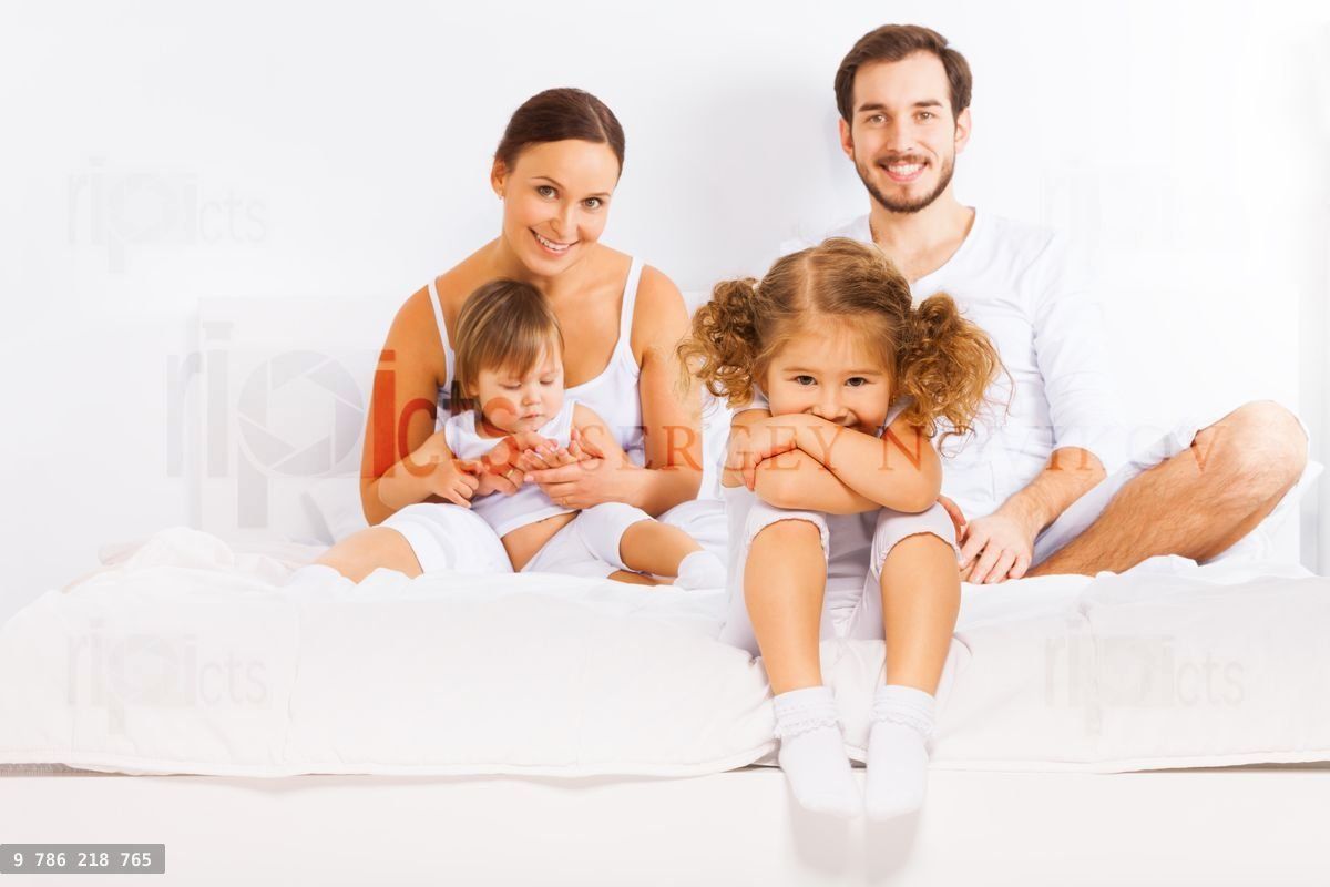 Family sitting on white bed in pajamas together