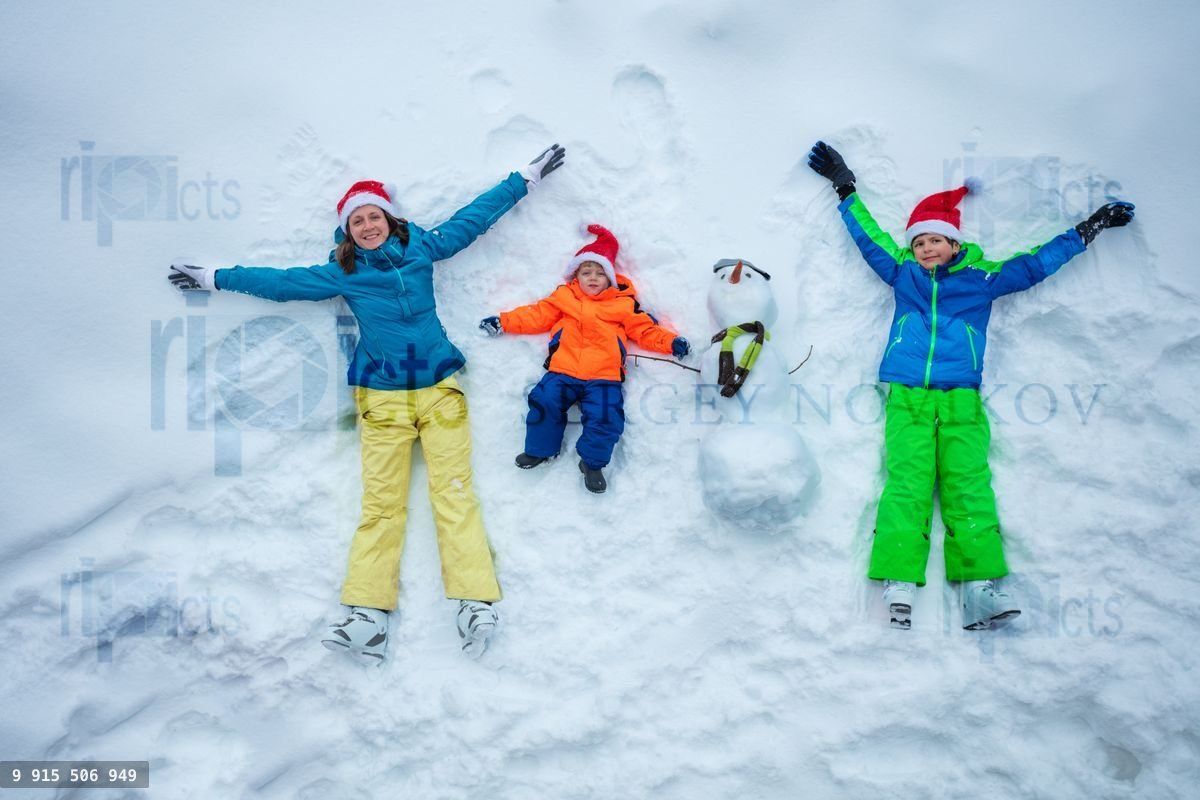 Mère et deux garçons en bonnet de Père Noël allongés avec un bonhomme de neige, vue de dessus