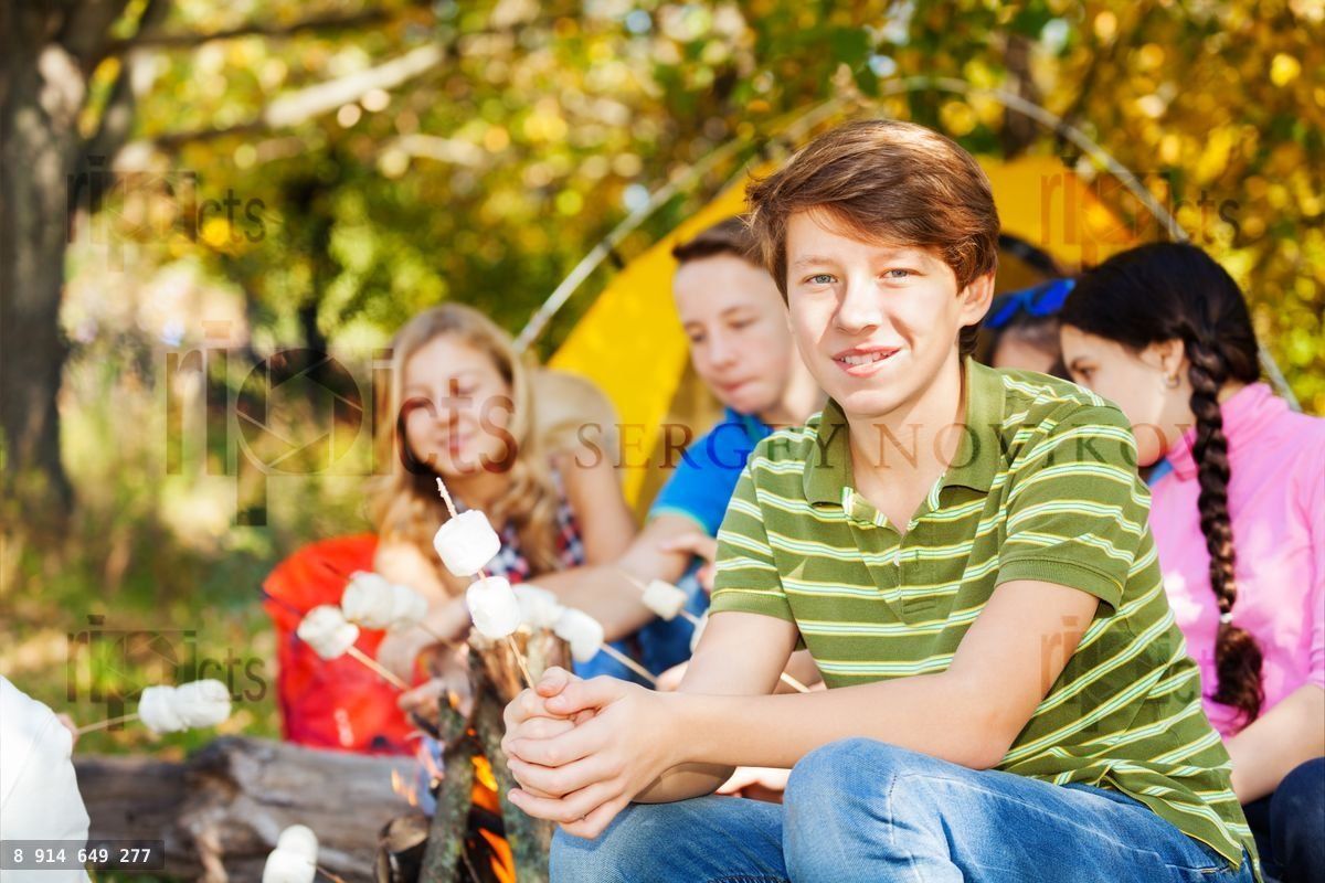 Friends hold marshmallow sitting on campsite