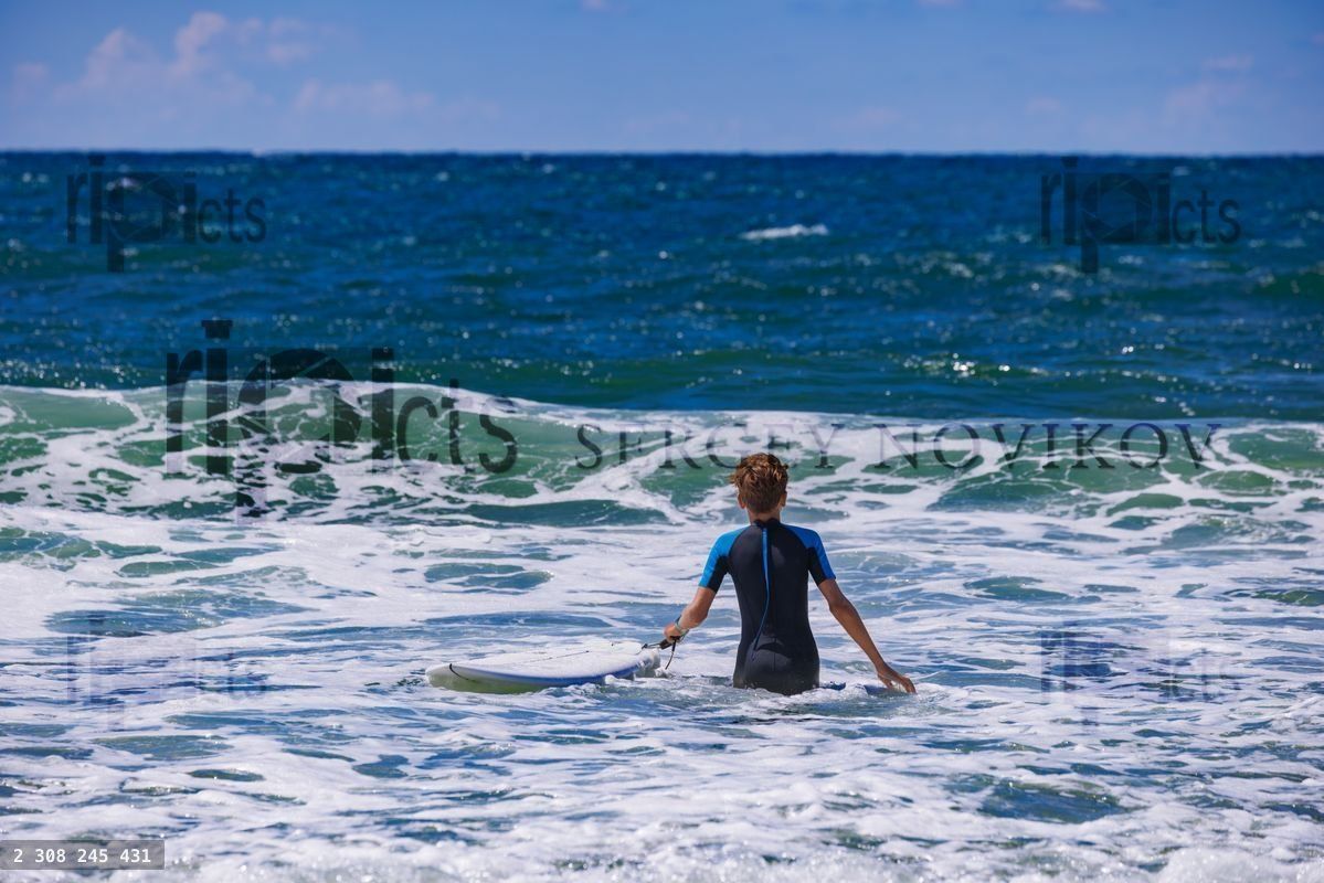 Young surfer in wetsuit walking into ocean waves on a sunny day
