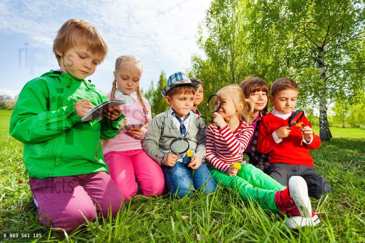 Group of kids sit in the field with magnifier