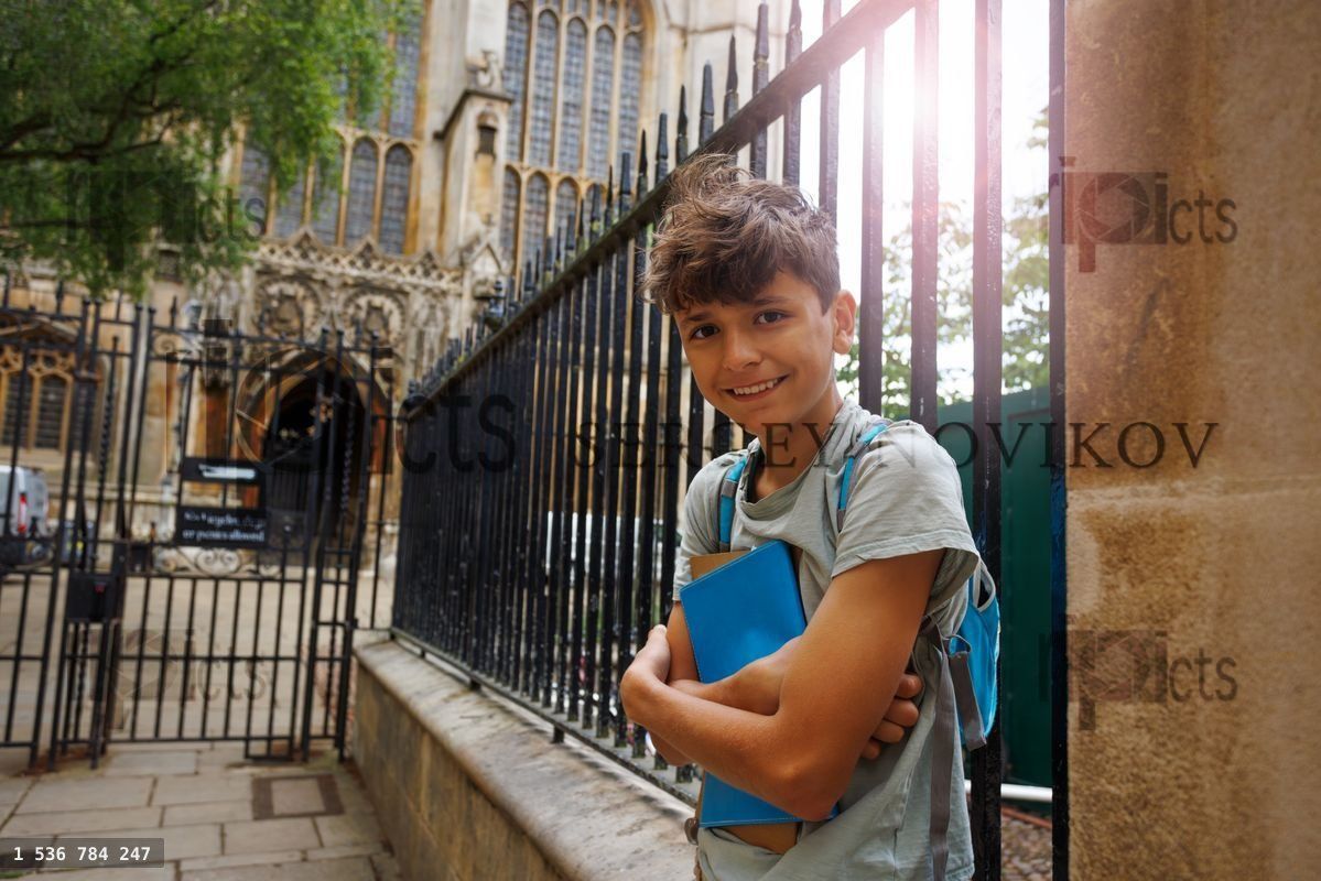 Young student with backpack near historic campus gate, Cambridge