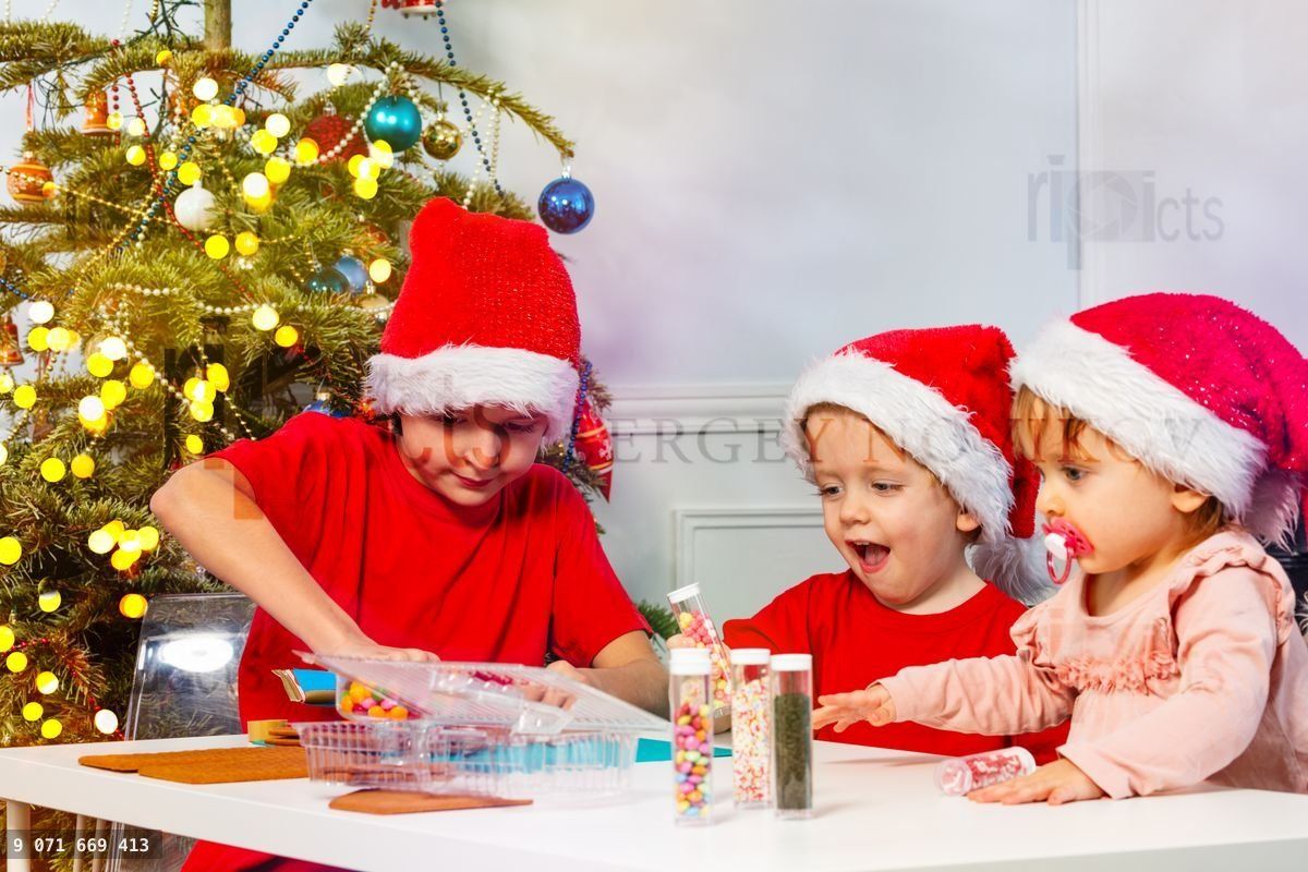 Trois enfants préparent une maison en pain d'épice avec des décorations
