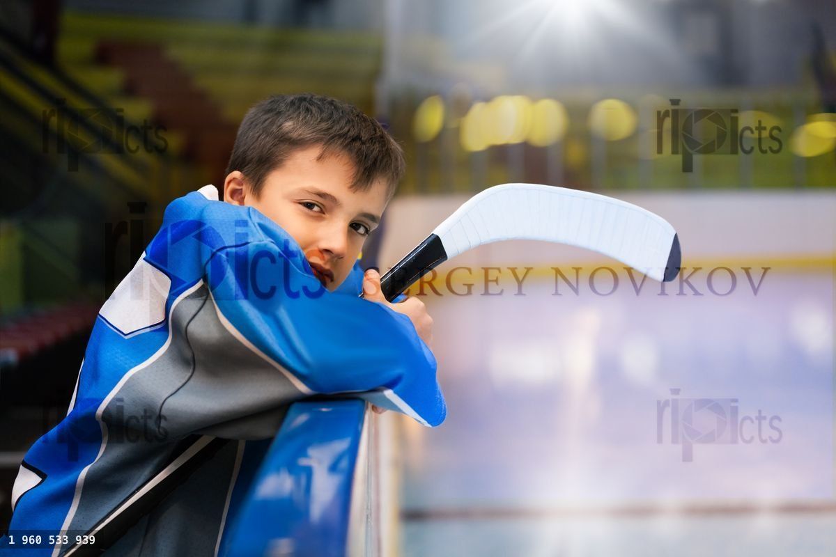 Young hockey player standing behind rink boards