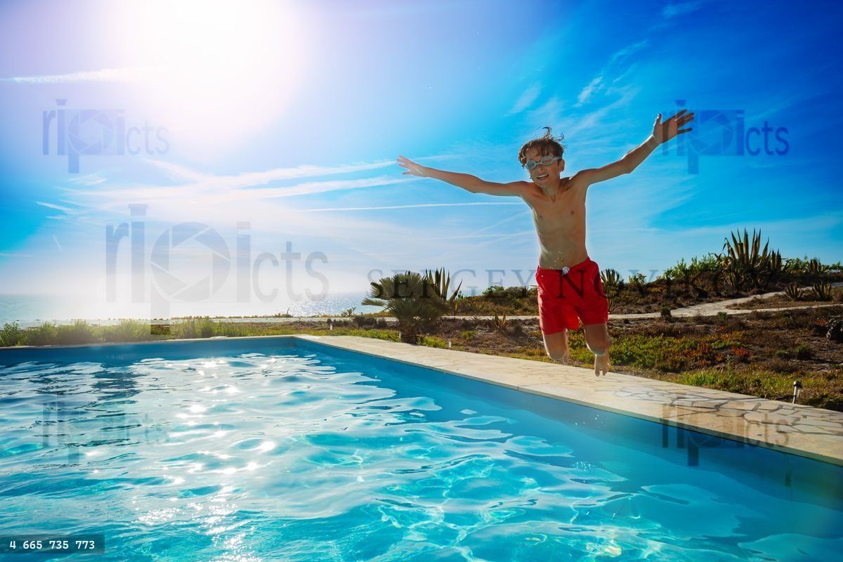 En dreng i røde badebukser hopper i swimmingpool med armen hævet