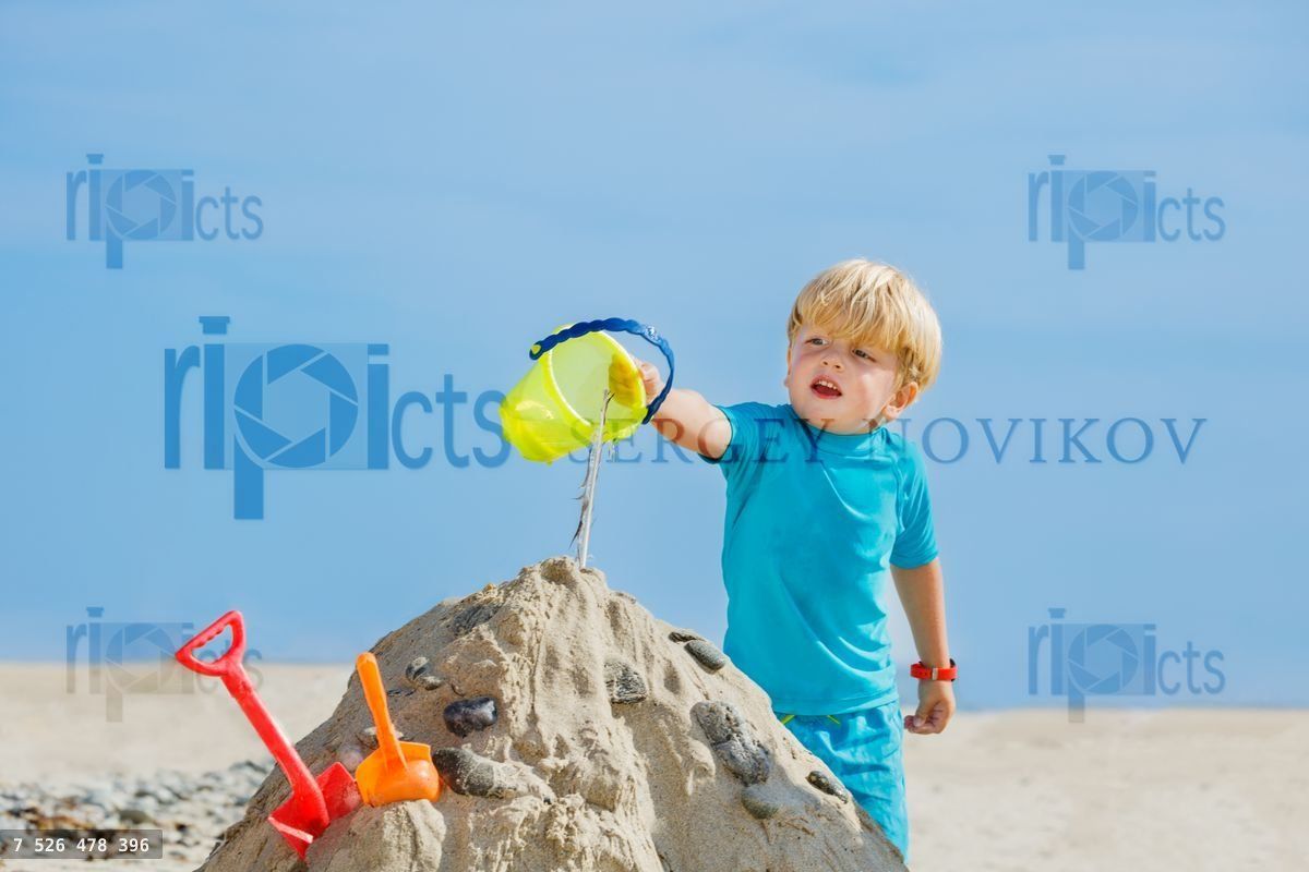 Handsome boy play with sand pouring water from plastic bucket