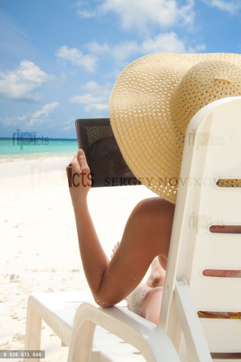 Woman sitting on the beach and browsing internet with tablet computer