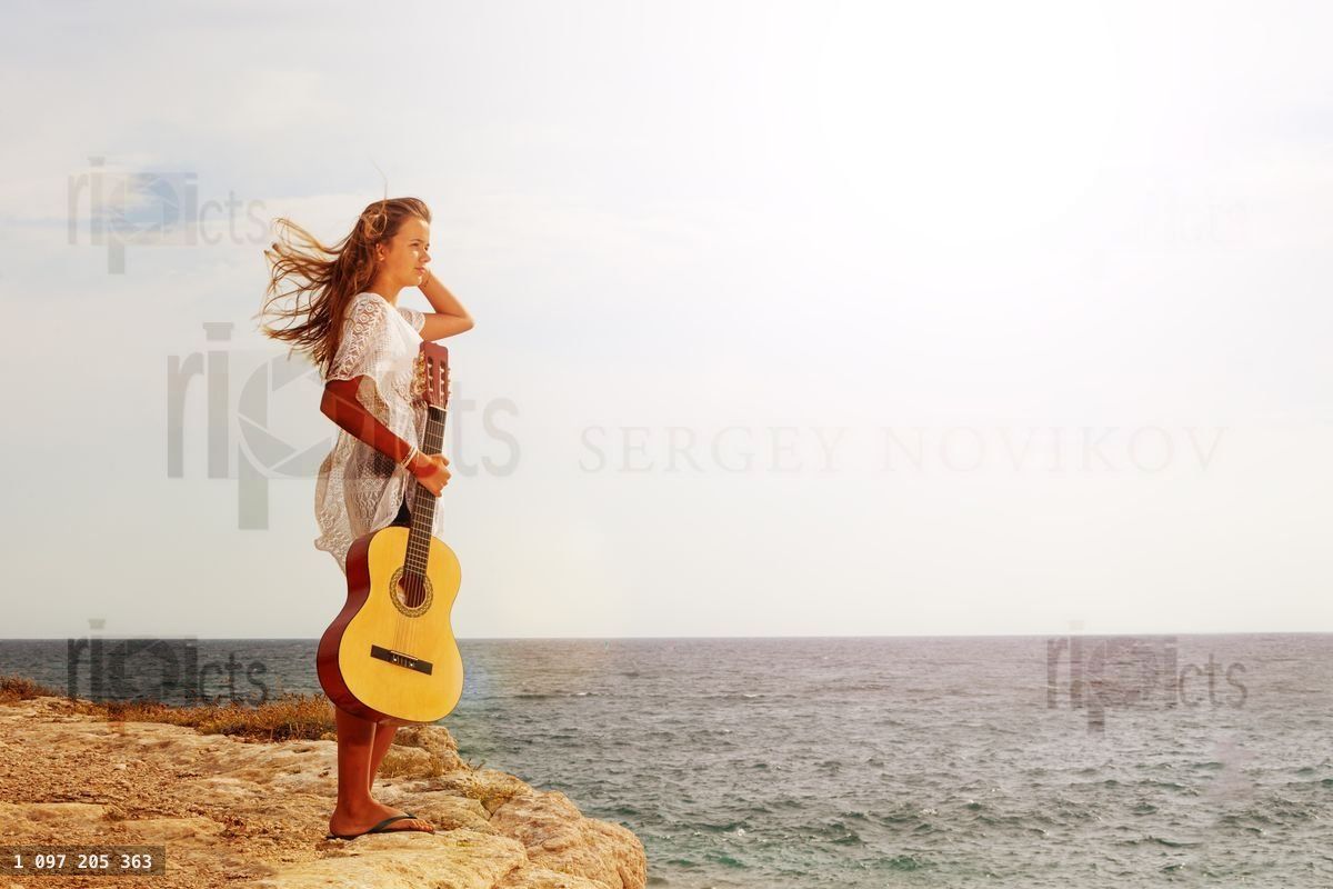 Young girl with guitar looking at the sea