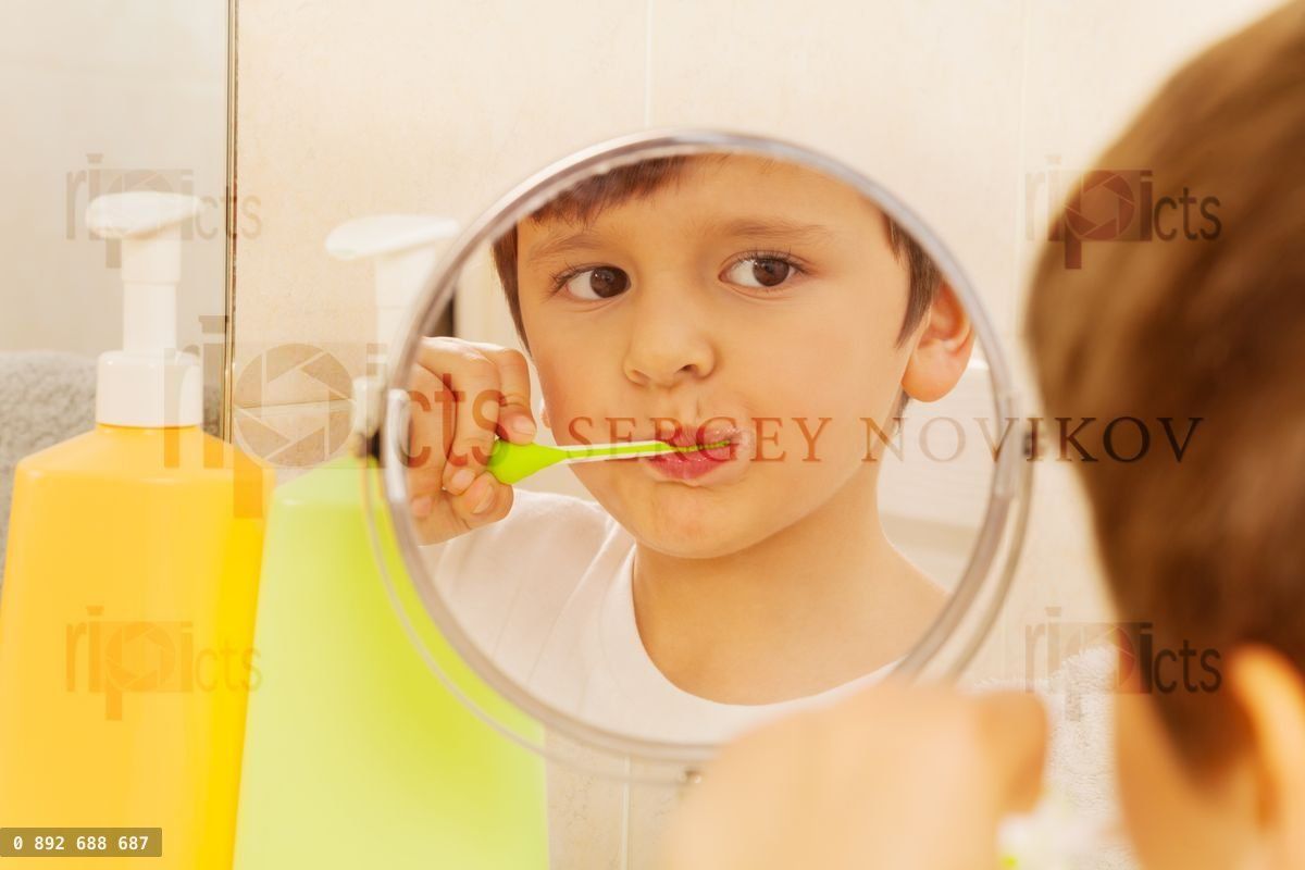 Cute boy looking in the glass and brushing teeth