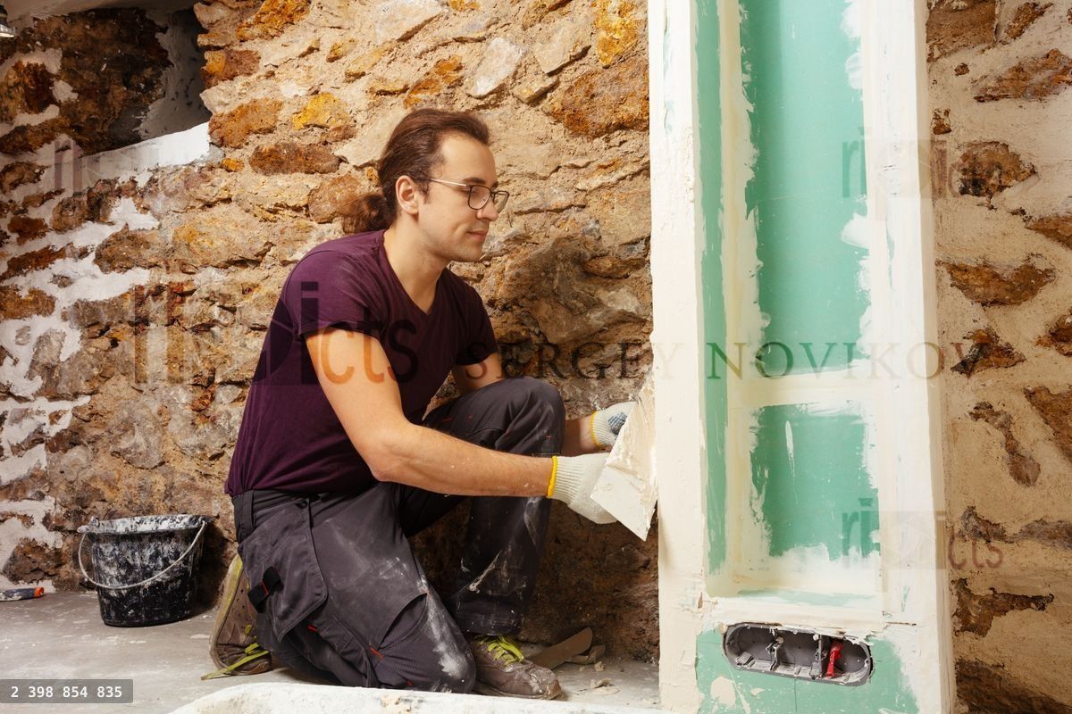 Young man working on plastering drywall at home renovation
