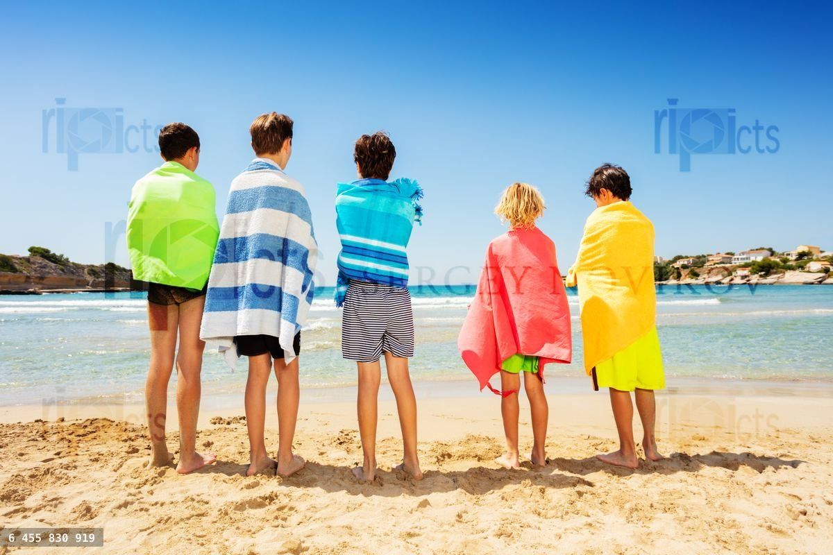 Friends wrapped in beach towels admiring seascape