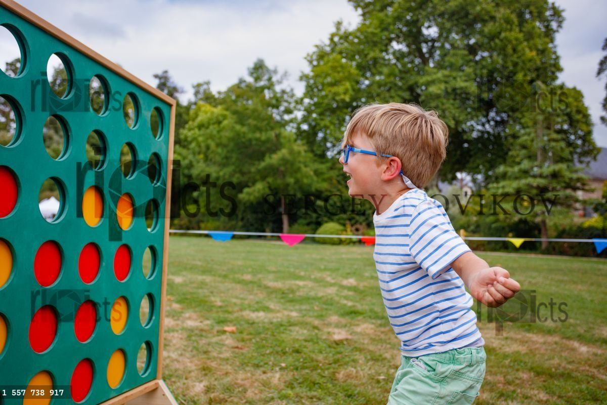Young boy in stripes plays Connect Four at the park on town fair