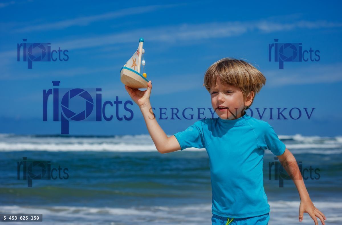 Young boy joyfully playing with toy sailboat at beach vacations