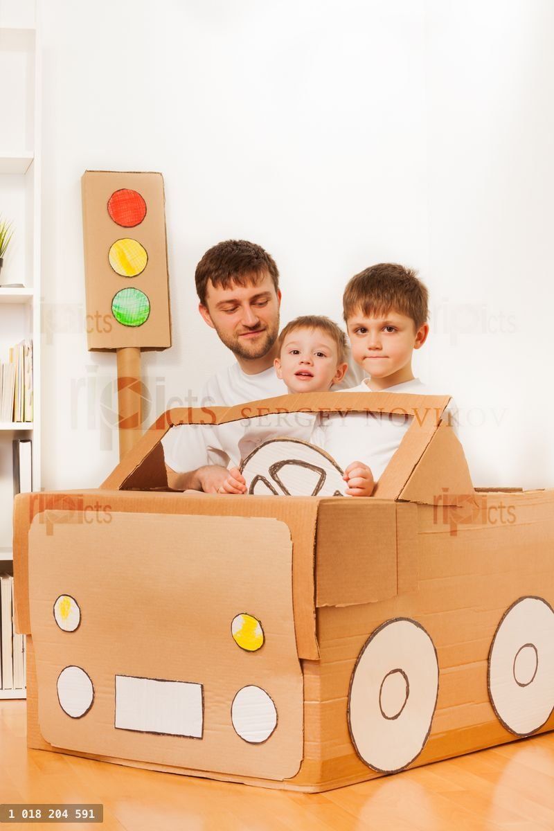 Boys driving dad in toy car made of cardboard box