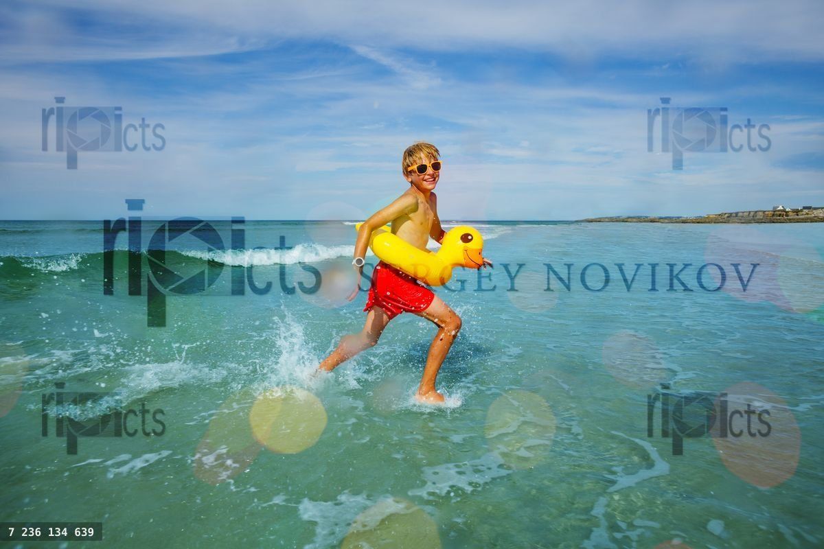 Happy boy run with inflatable duck in ocean at the beach