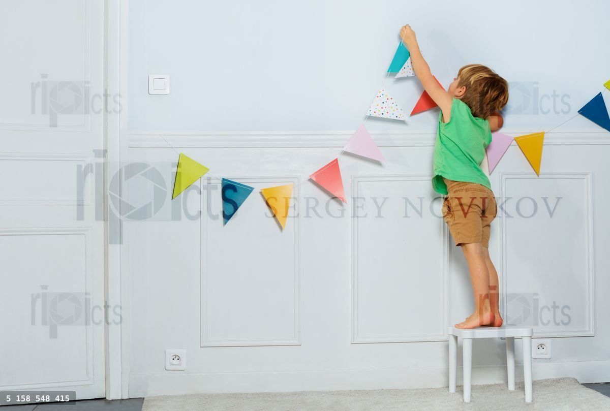 Young boy hangs birthday garland with flags on living room wall