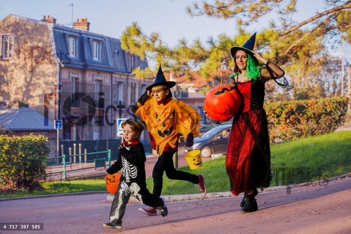 Mère avec des garçons courant dans des costumes d'Halloween dans la rue de la ville