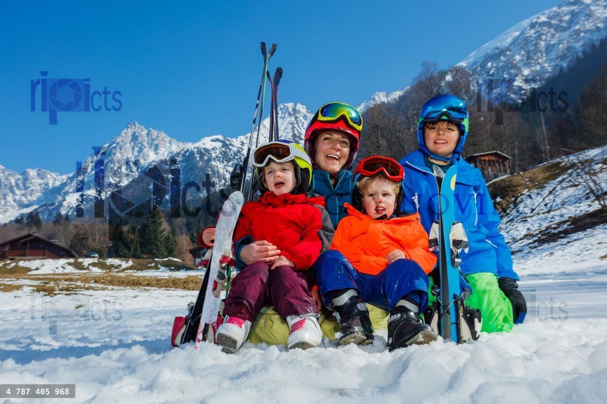 Mother with small kids sit in the snow wear ski outfit