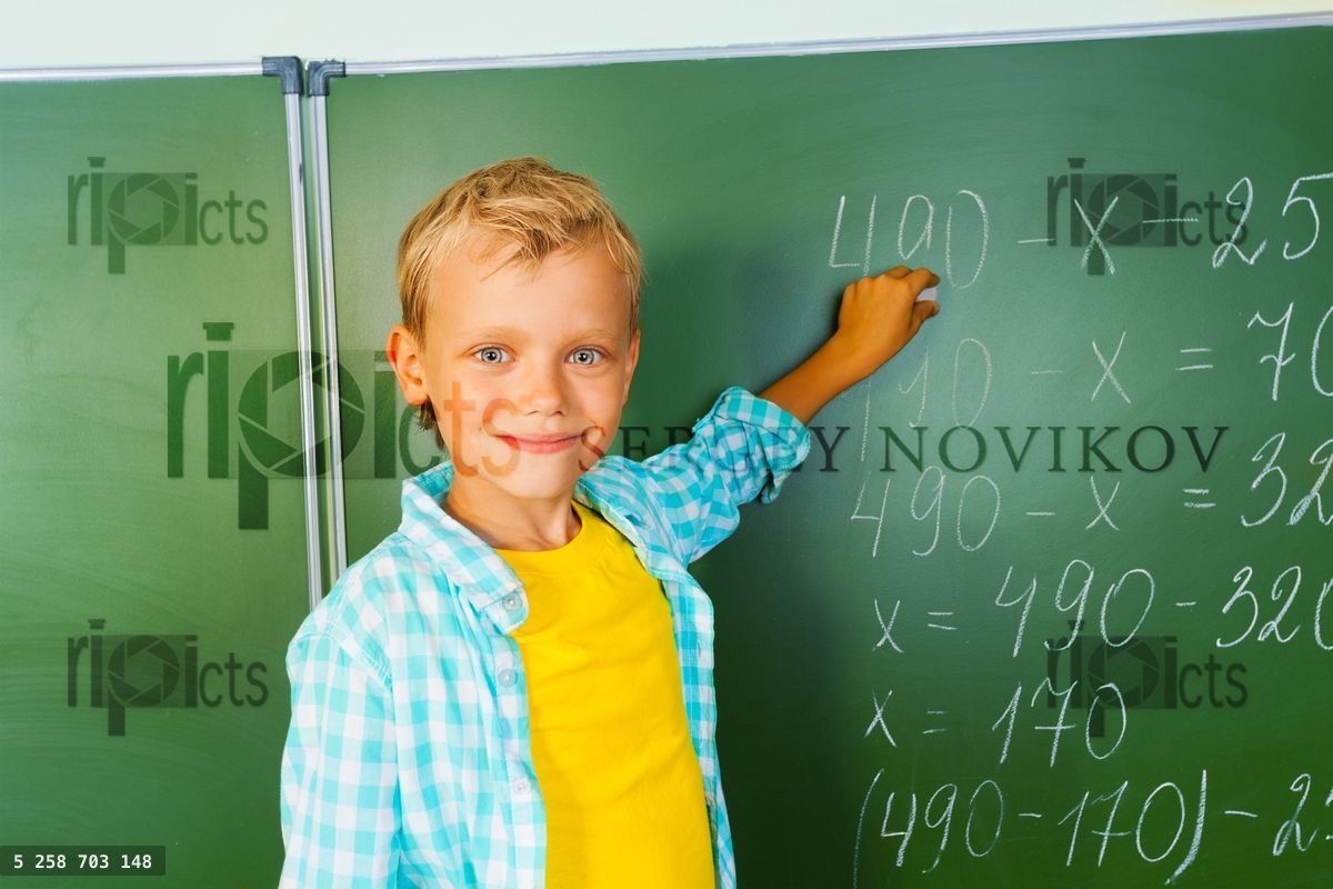 Boy with chalk stands near blackboard and looking
