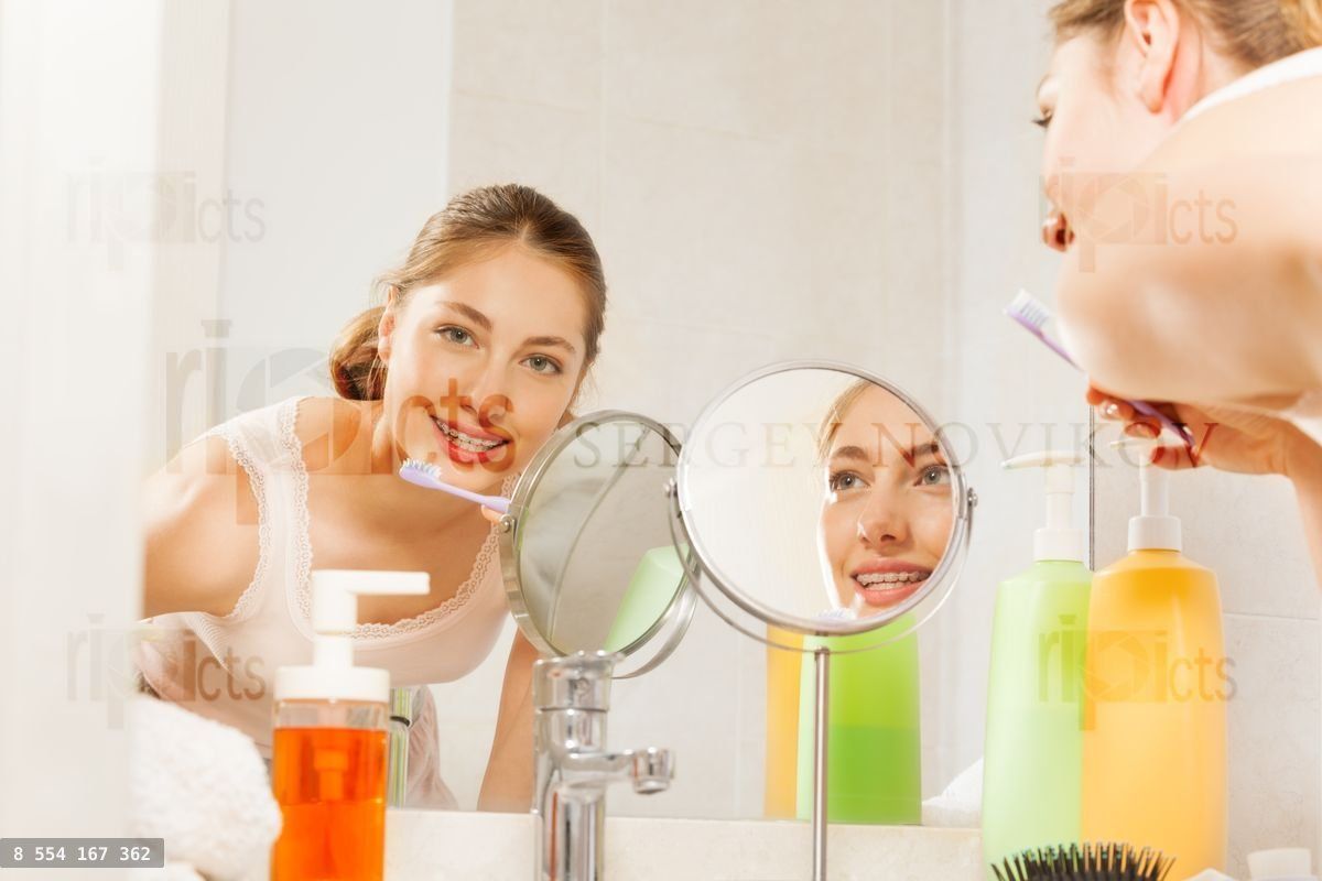 Woman brushing her teeth seen in bathroom mirror