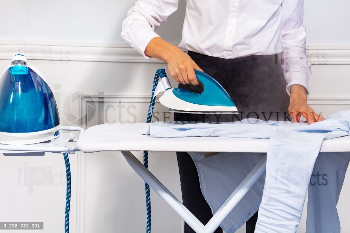 Woman's hand holding steam iron and ironing shirt