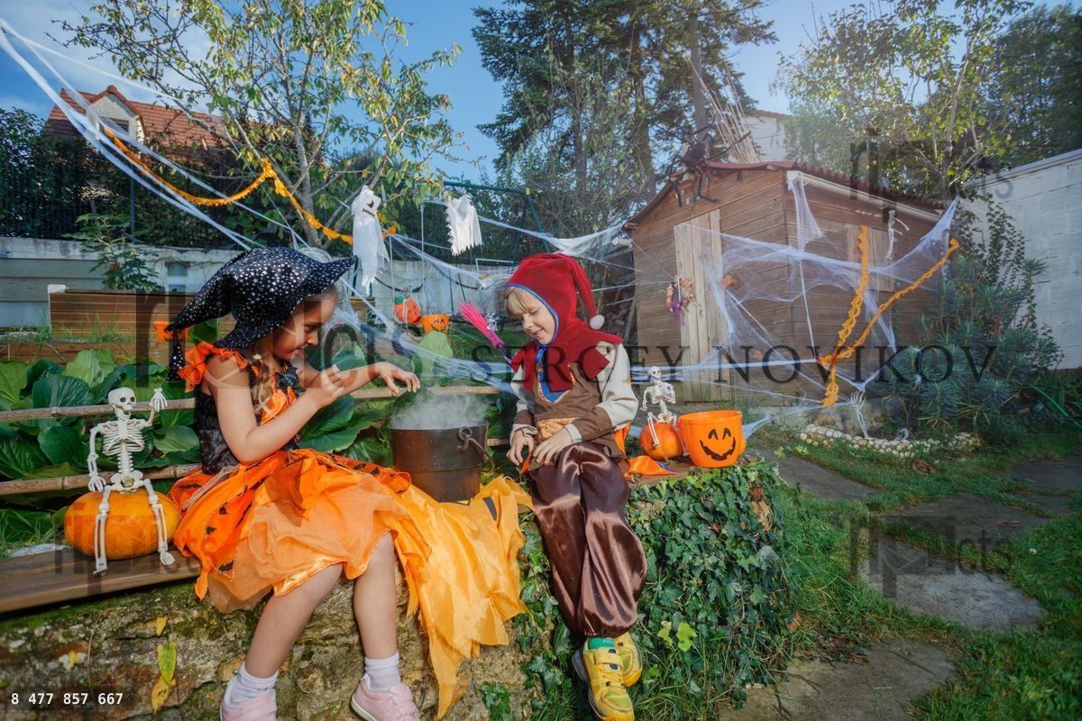 Twee kinderen in Halloween-kostuum zitten bij een stoomende zwarte ketel