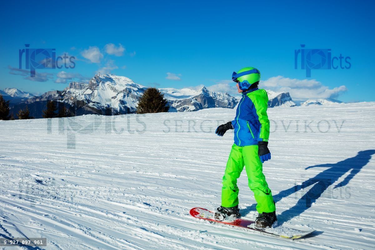 Snowboarder boy go downhill on snowboard from mountain top