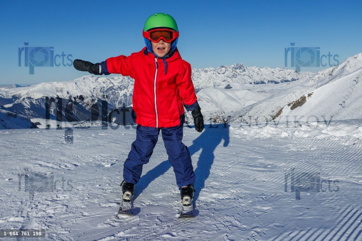 Boy in red jacket stands with arms out on snowy ridge today