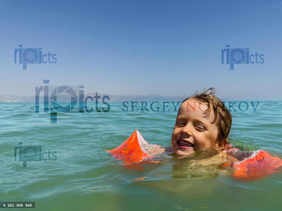 Young swimmer boy enjoys the ocean in bright orange arm bands
