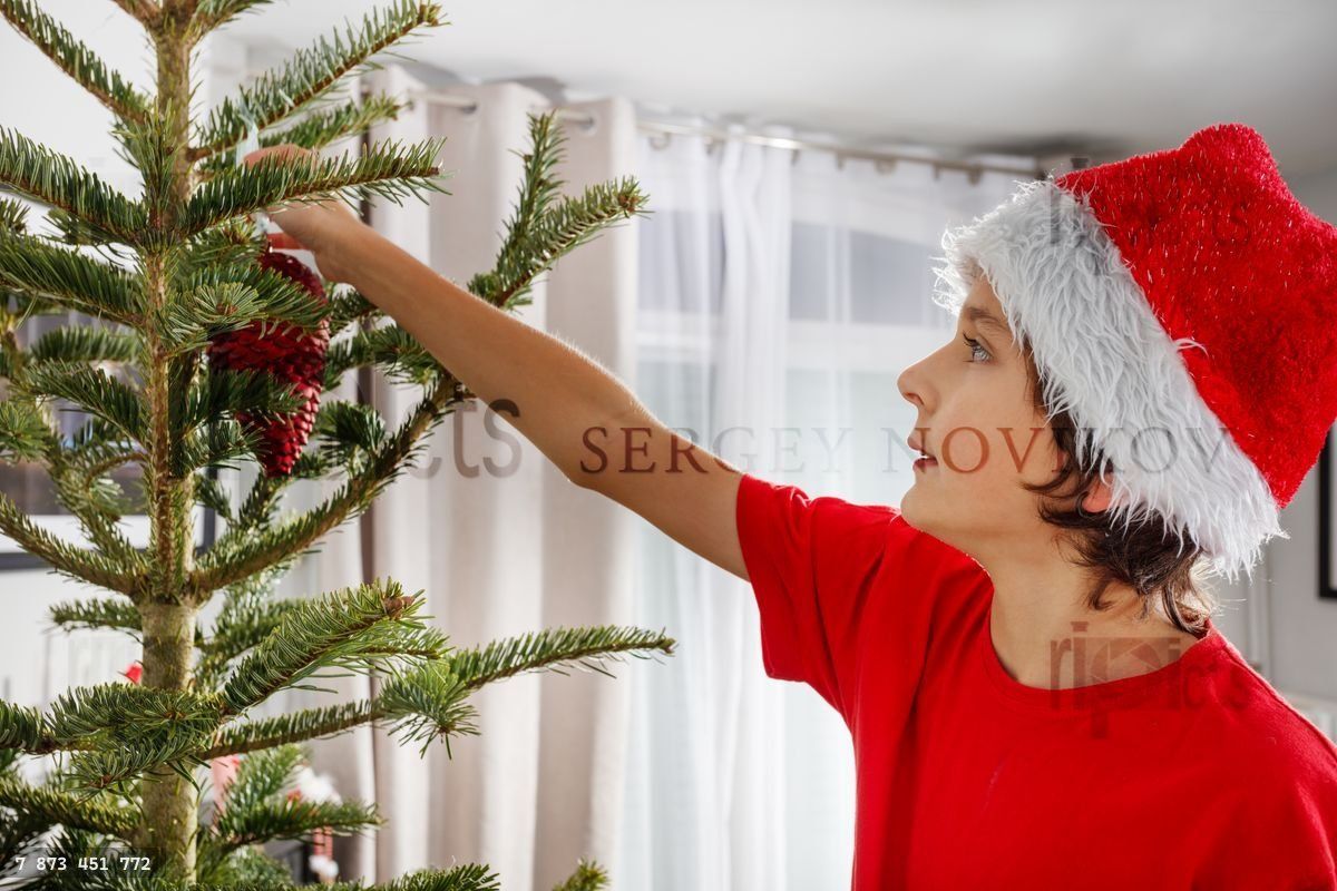 Jeune garçon en bonnet de Père Noël accrochant des ornements sur le sapin de Noël
