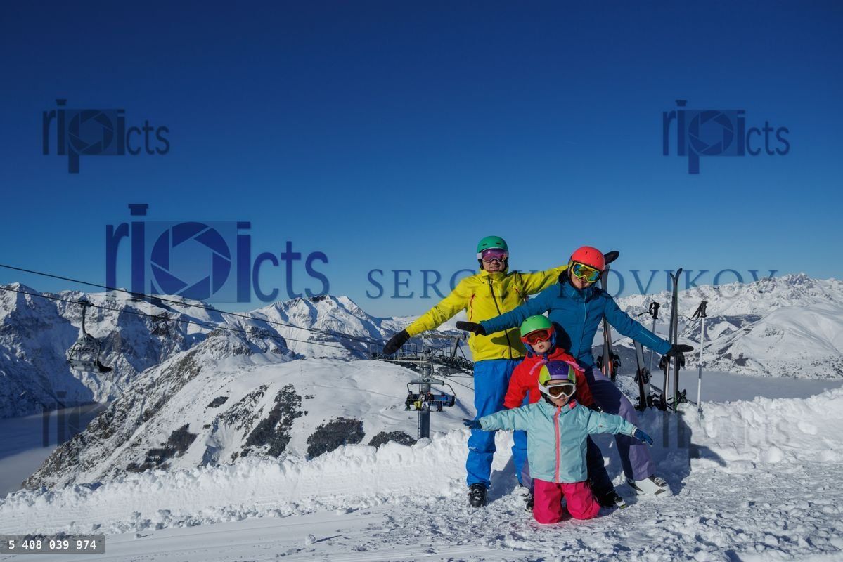 Four people pose with skis on a snowy mountain under clear skies
