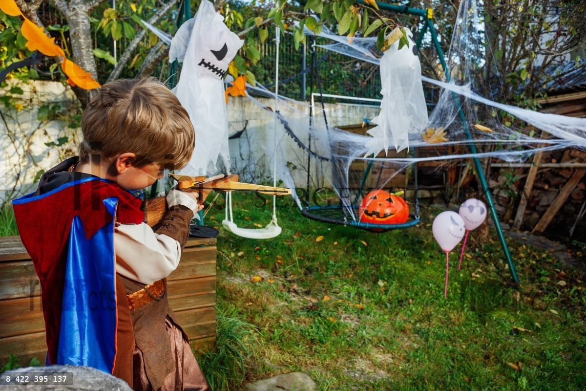 Young knight with wooden bow celebrates Halloween aiming pumpkin