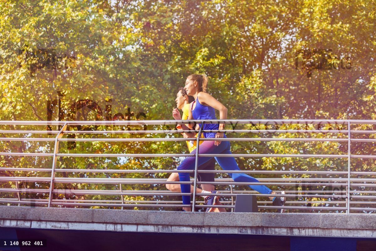 Young couple running across a bridge at city park