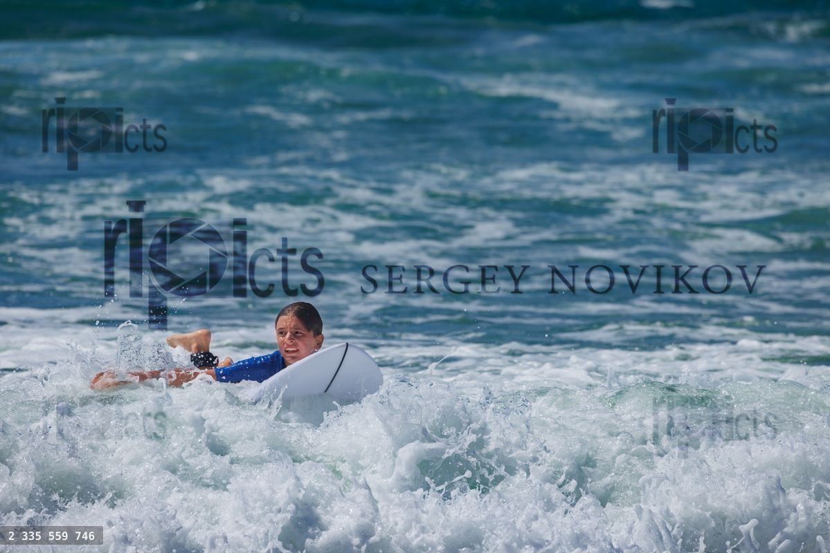 Young surfer boy wait for ocean waves laying on his surfboard