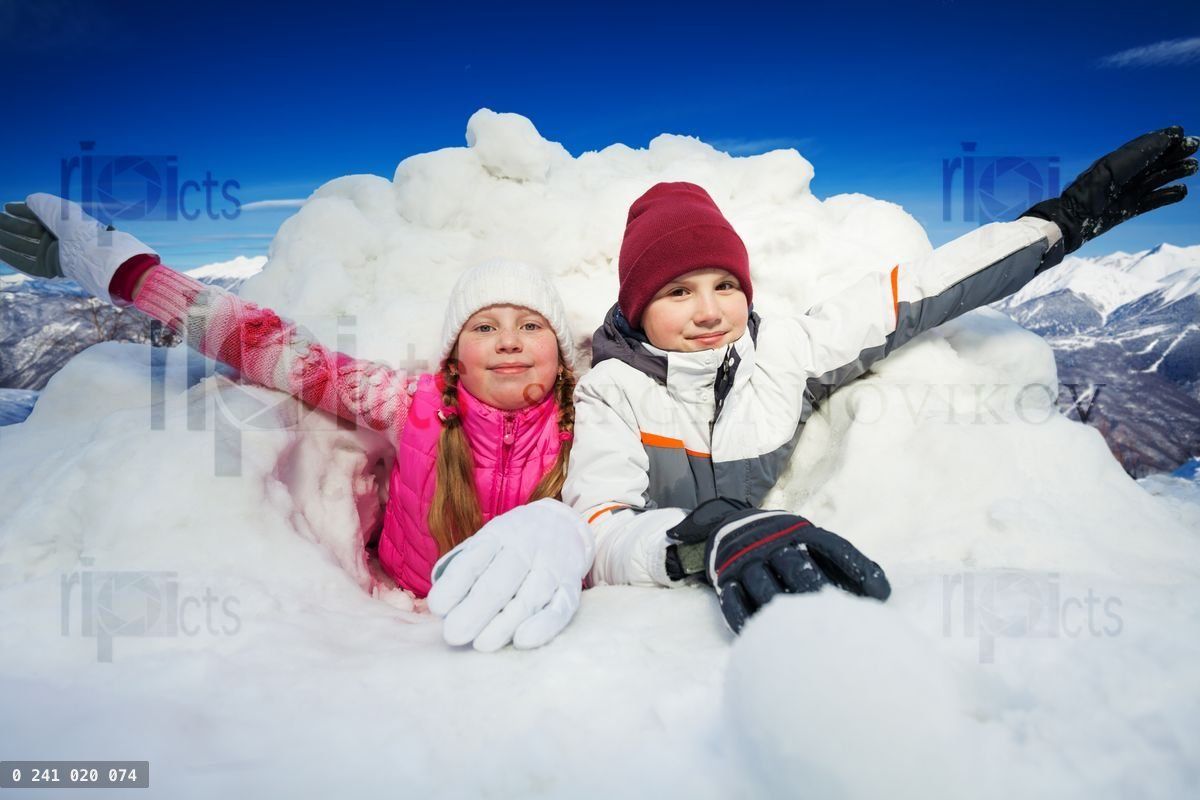 Happy children at snow cave outside in winter time