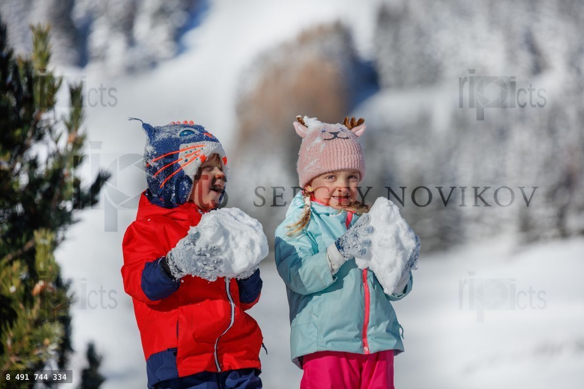 Two children grin holding snowballs against a snowy backdrop