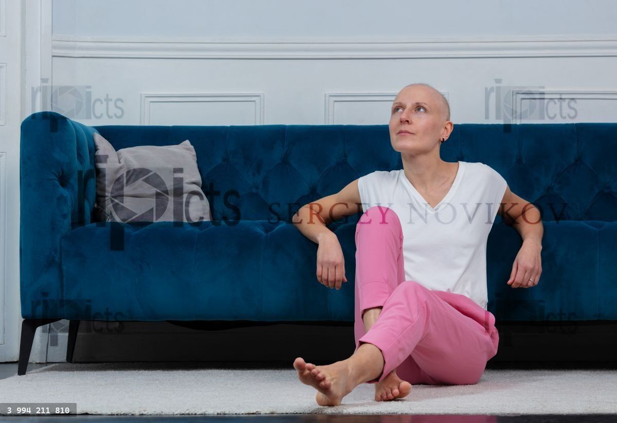 Woman fighting cancer with sitting thoughtfully by a blue couch
