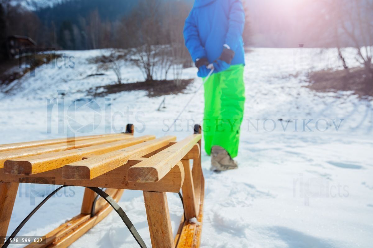 Wooden sledge closeup pulled by a boy uphill the snow mountain