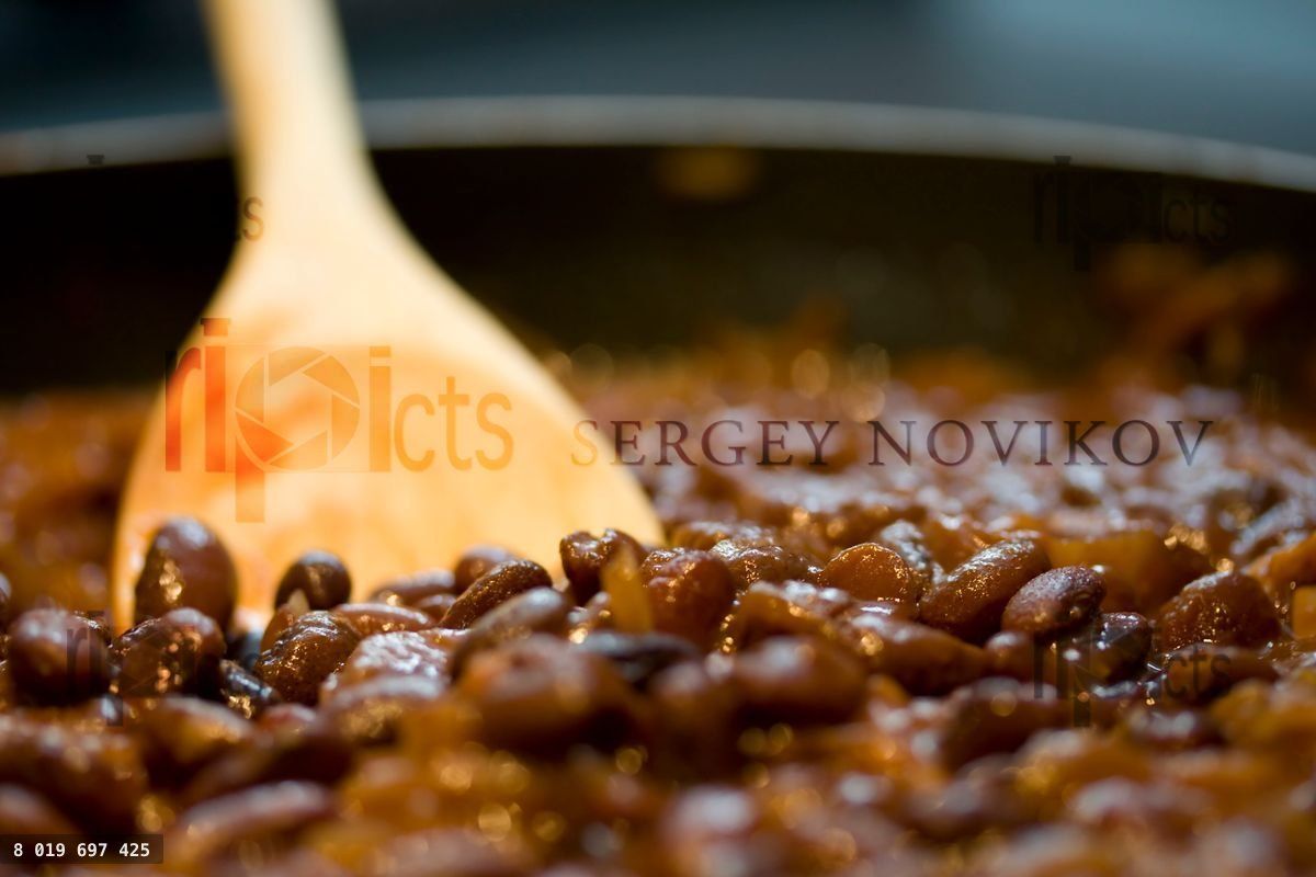 Wooden spoon stirring baked beans in savory sauce