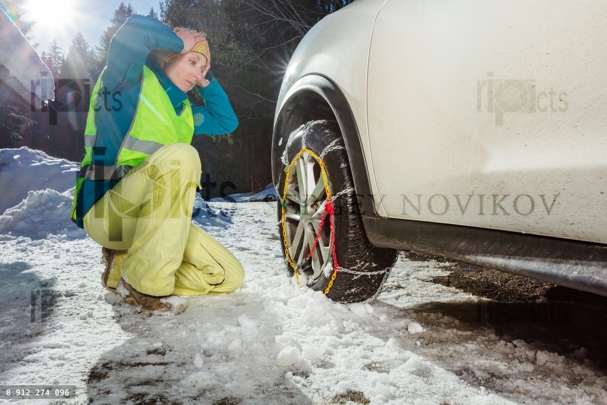 Woman hold head with hands trying to put chains on the car