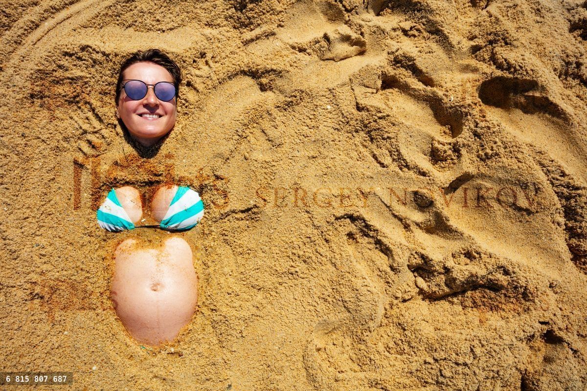 Belly of happy pregnant woman buried in the sand
