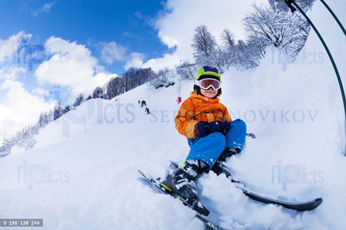 Child with ski and wearing mask sit in snow