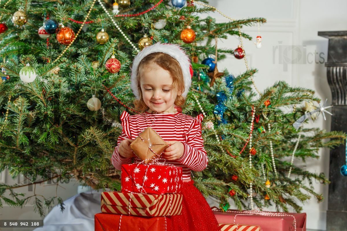 Happy girl unwrap her holiday presents by the Christmas tree
