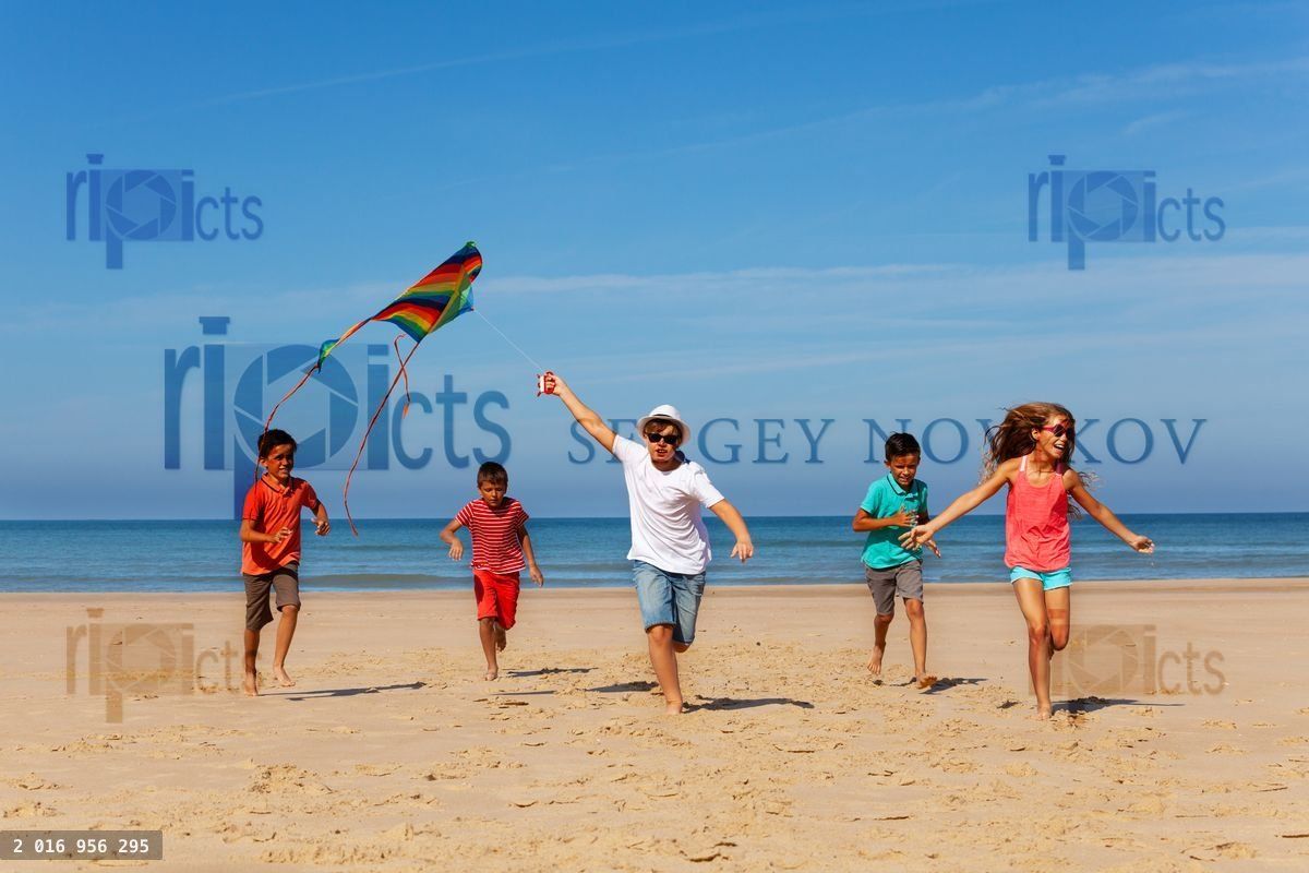 Group of many kids run with kite on a sand beach