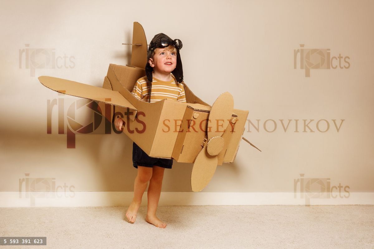 Young boy hold cardboard plane wears hat, glasses, pretends fly