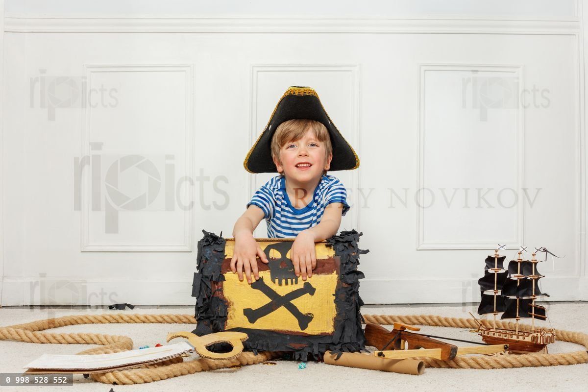 Young pirate boy playing with treasure chest and ship at home